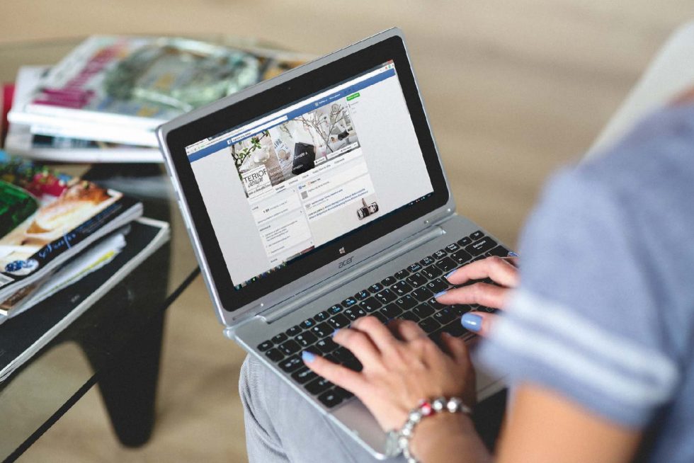 woman's hand typing on laptop. Laptop is on Facebook page.